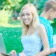 Happy girl with a laptop and a student on the background at the park