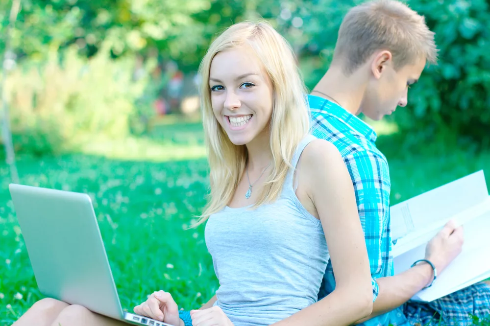 Happy girl with a laptop and a student on the background at the park